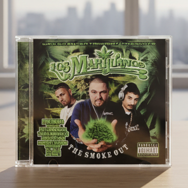 A CD case for the album 'The Smoke Out' by Los Marylindo, displayed on a wooden surface with a blurred window and city skyline in the background.