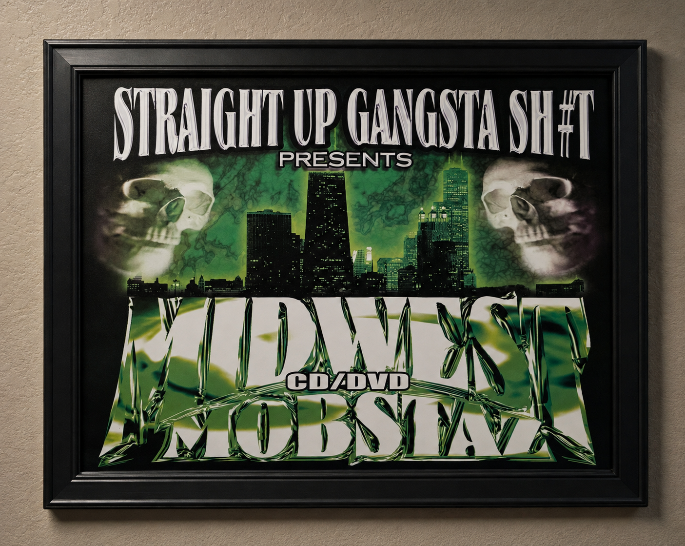 A framed music CD/DVD cover for 'Midwest Mobsta' presented by 'Straight Up Gangsta Sh*t', featuring a green and black city skyline with skull graphics, mounted on a beige wall.